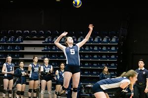 Young woman serving the volleyball while teammates watch on the sidelines